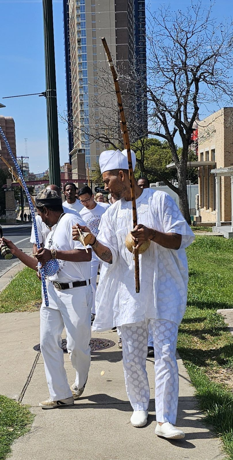 Capoeira Angola practitioners in white playing berimbau and percussion outdoors in Austin