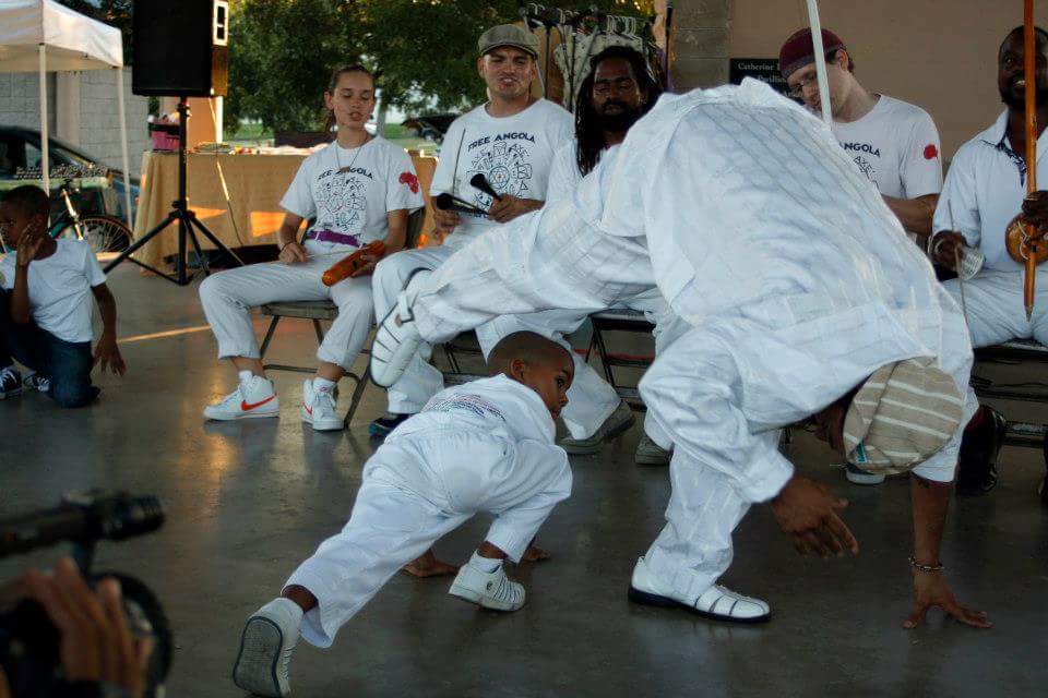 A child and an adult playing capoeira angola at a community event