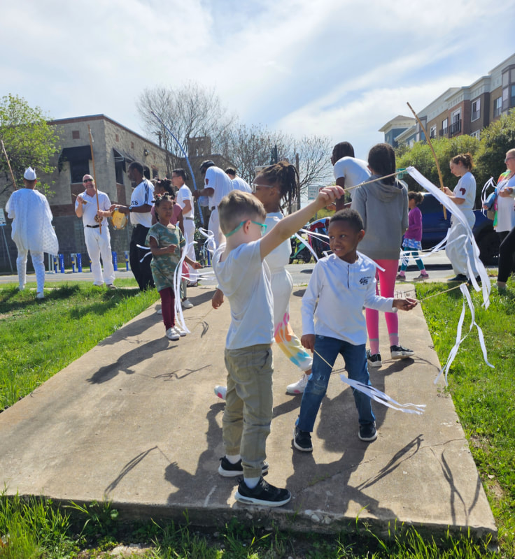 Children waving ribbons outdoors during a community capoeira celebration