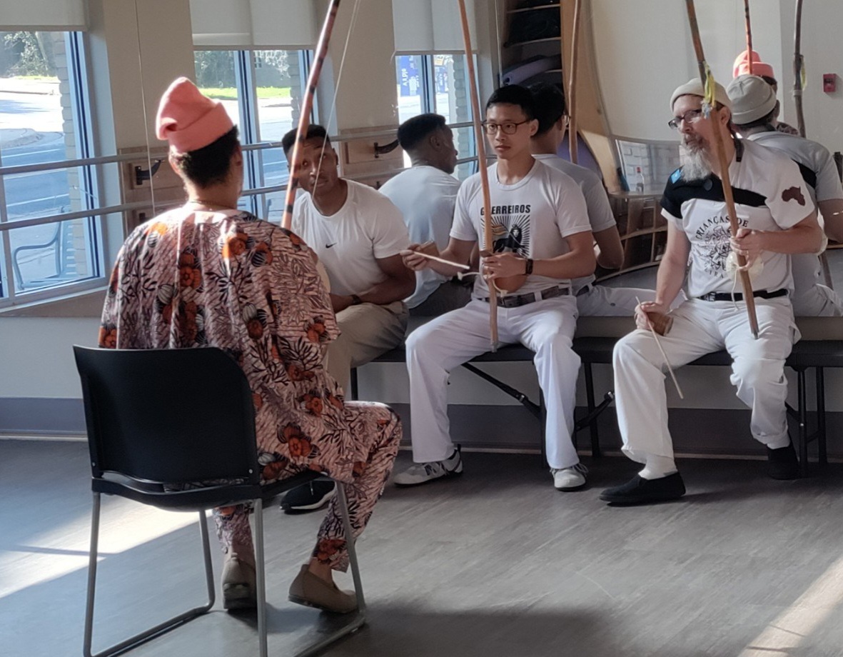 Students in white holding berimbaus during a music class with the founder